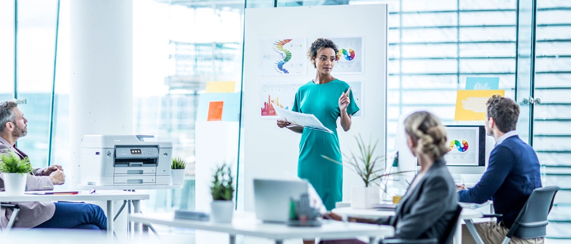 A woman standing in front of a mood board addressing three colleagues 