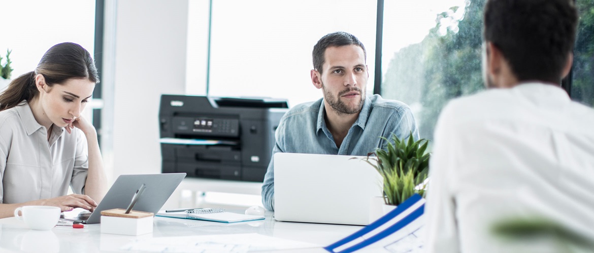 Three colleagues collaborate with laptops in front of Brother A3 Inkjet Printer