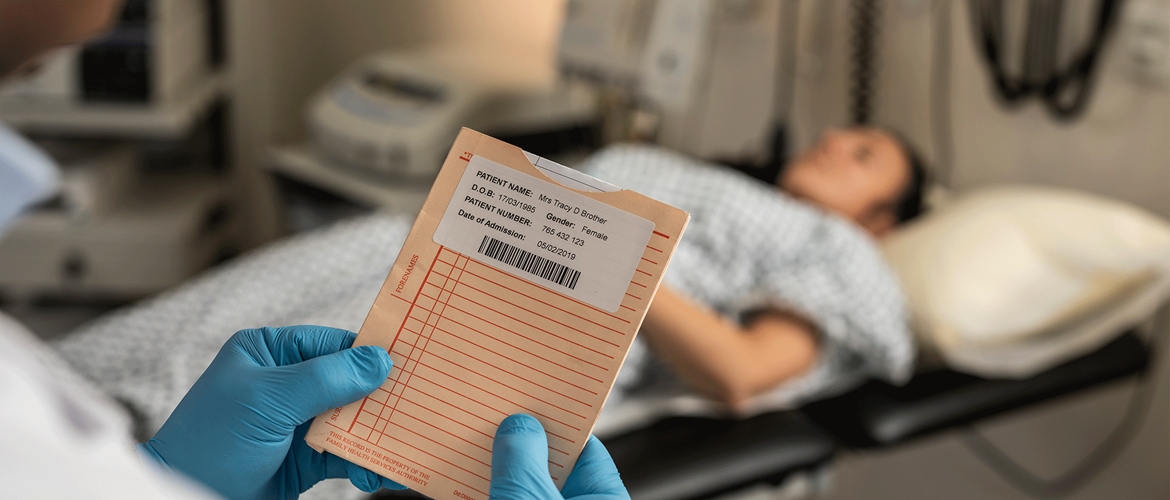 Pacientka ležiaca na nemocničnej posteli, doktor kontrolujúci záznamy